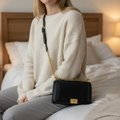 Black Royal sling bag of Vella Luxe with a girl hanging bag and sitting on white bed 
